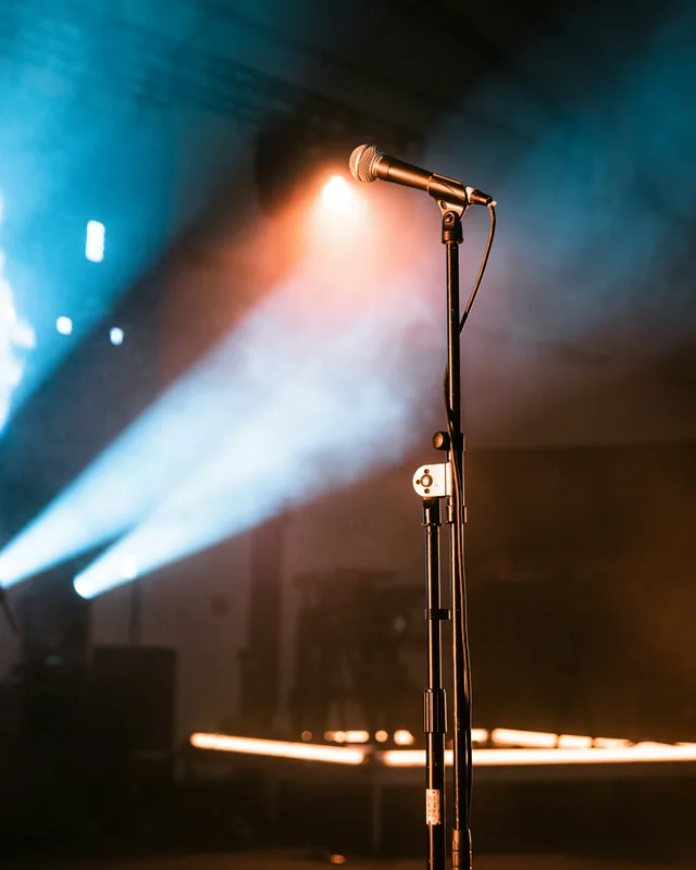 Vocal microphone on a stand under cool stage spotlights at a live show.