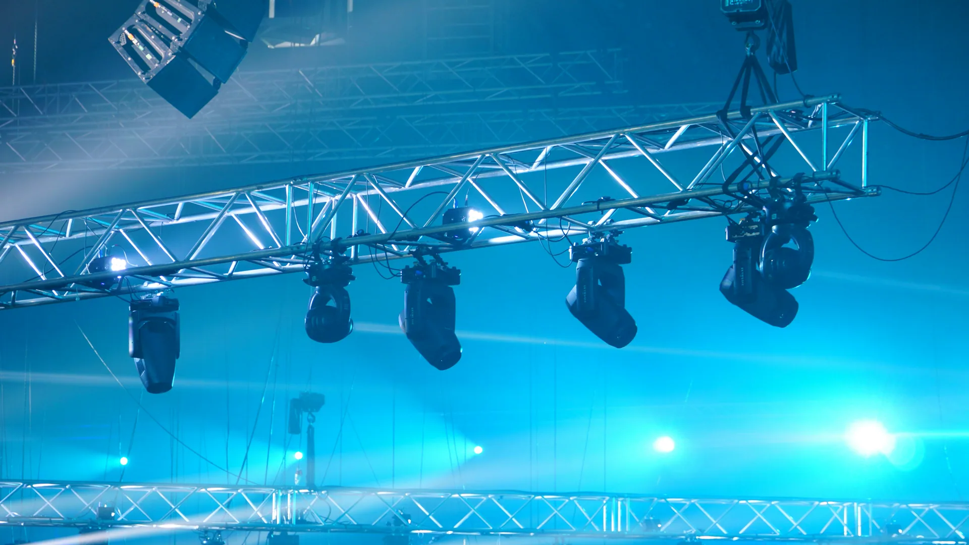 Lighting truss with moving fixtures cutting blue beams through theatrical haze.