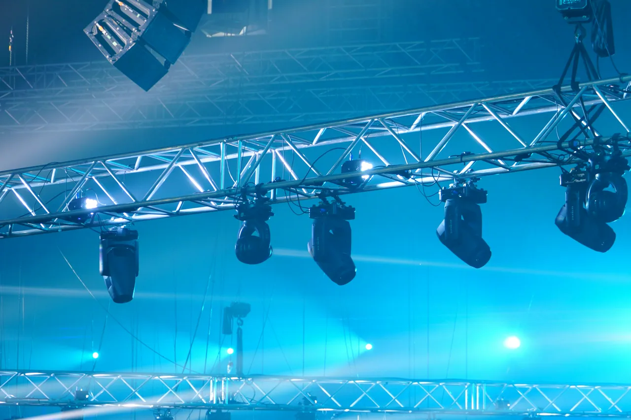 Lighting truss with moving fixtures cutting blue beams through theatrical haze.