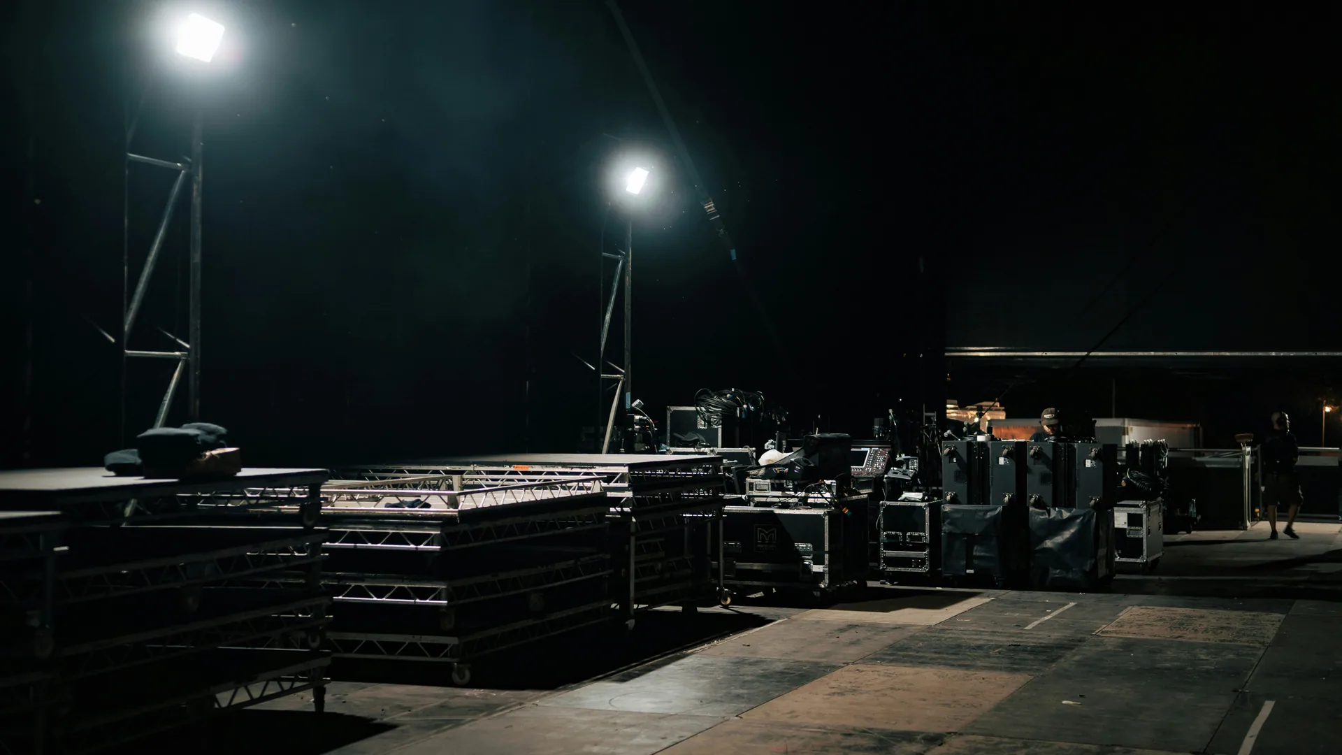 Backstage staging area at night — flightcases, truss, work lights, ready for load-in.