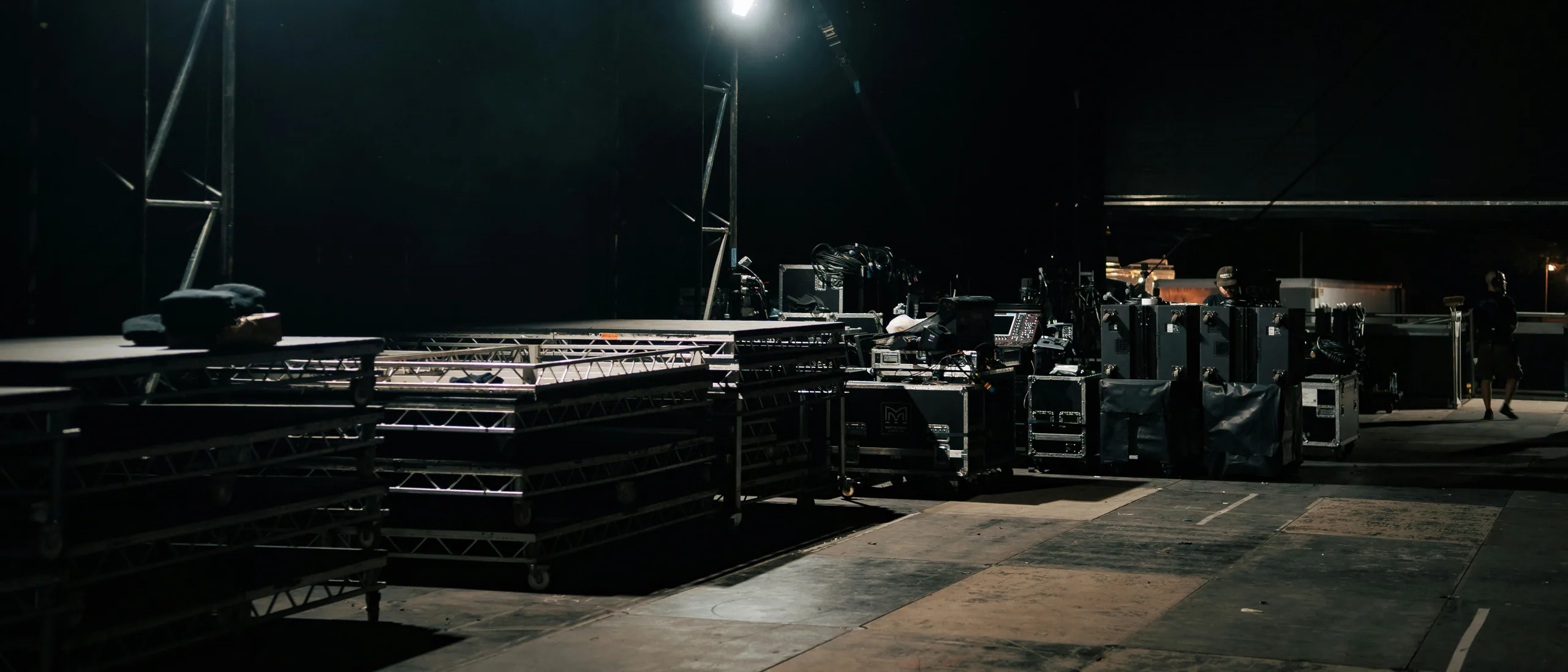 Backstage staging area at night — flightcases, truss, work lights, ready for load-in.